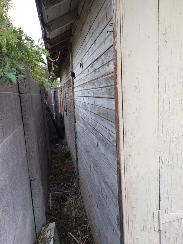 A narrow alleyway with a wooden building and a brick wall.
