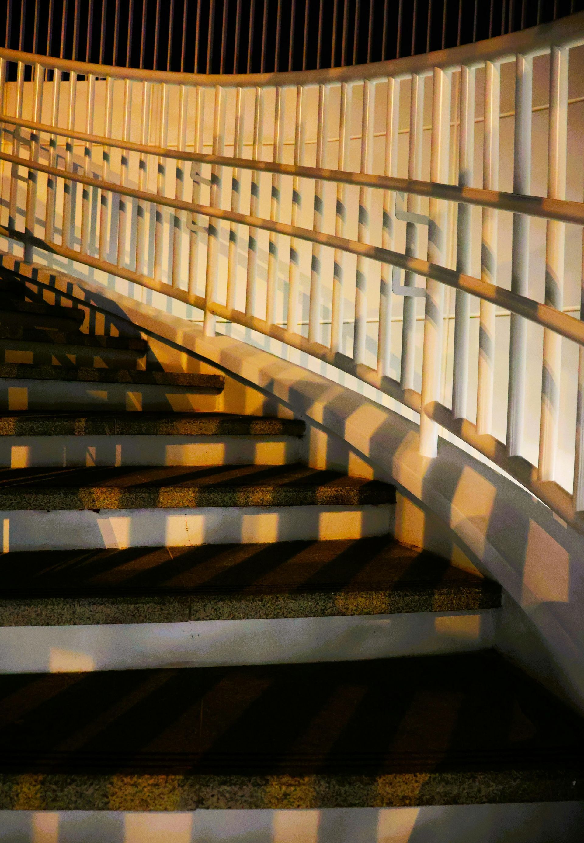 Staircase with white railing, lit by warm light, casting long shadows on steps.