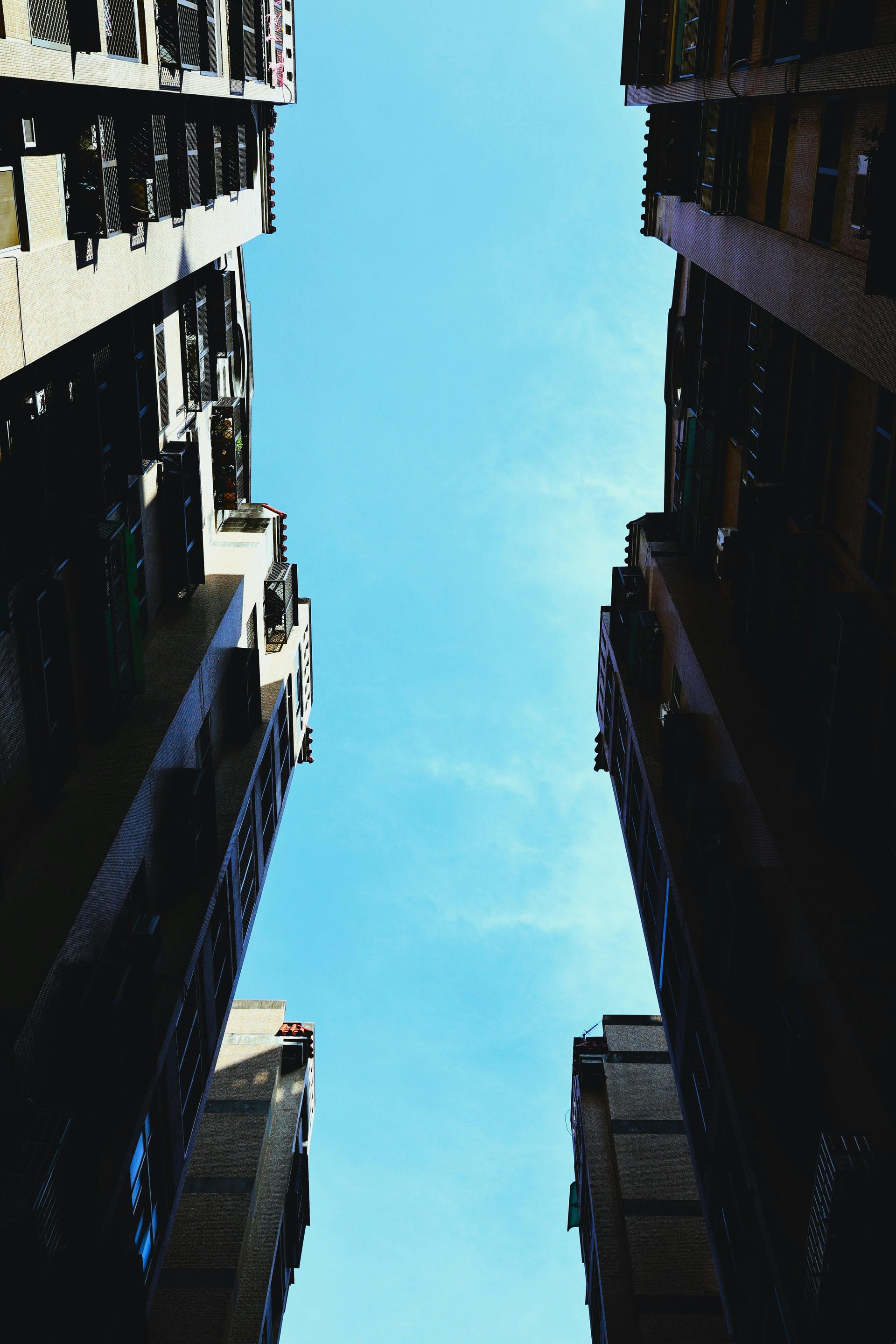 Looking up between tall buildings, clear blue sky above.