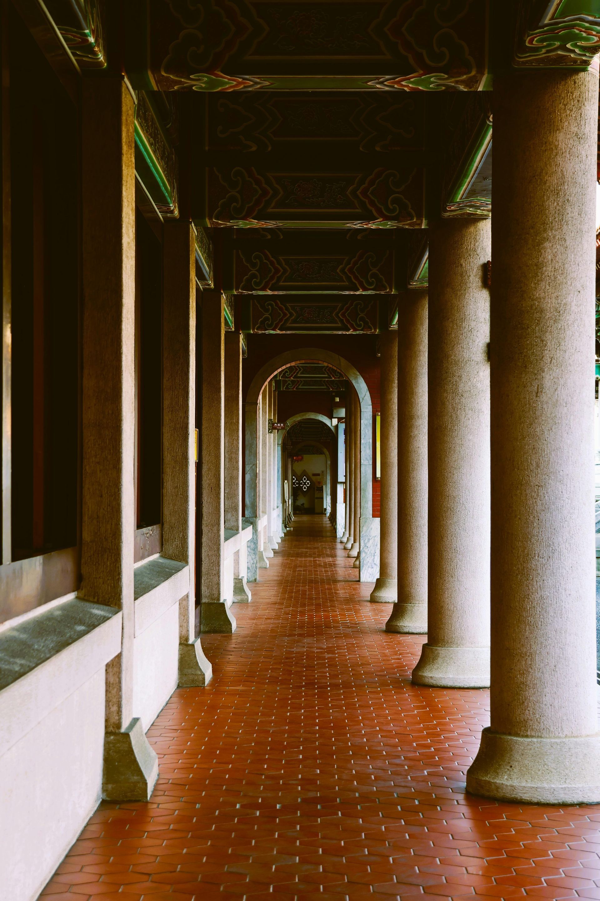 Covered walkway with red brick floor, stone columns, and arched ceiling.