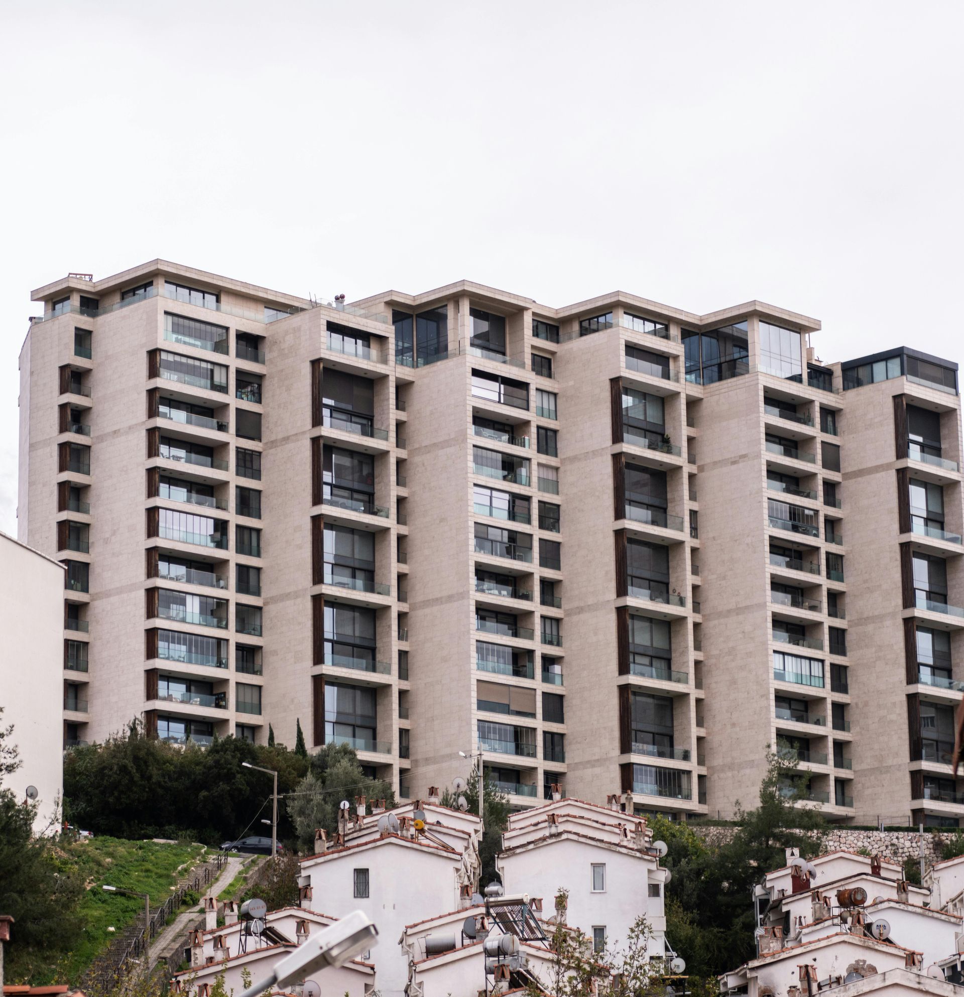 Multi-story apartment building with beige facade, overlooking white-roofed houses on a hillside.