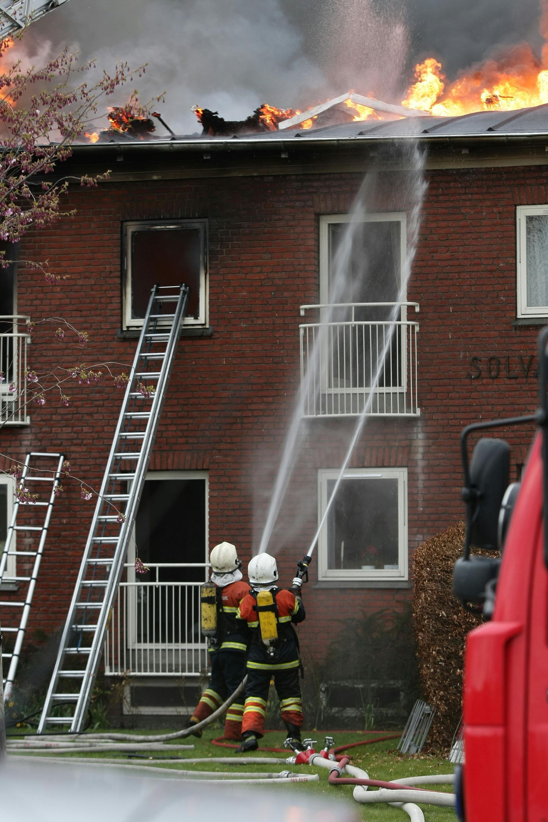 Firefighters battling a house fire, spraying water on the burning roof.