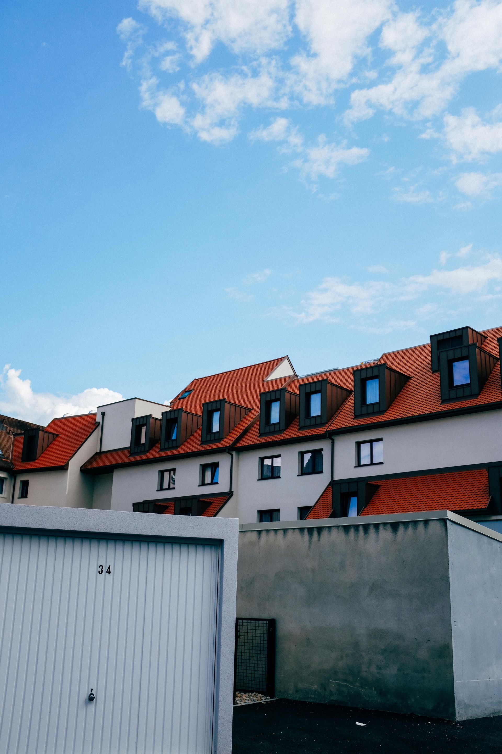 White building with orange tiled roof under blue sky, garage doors in foreground.