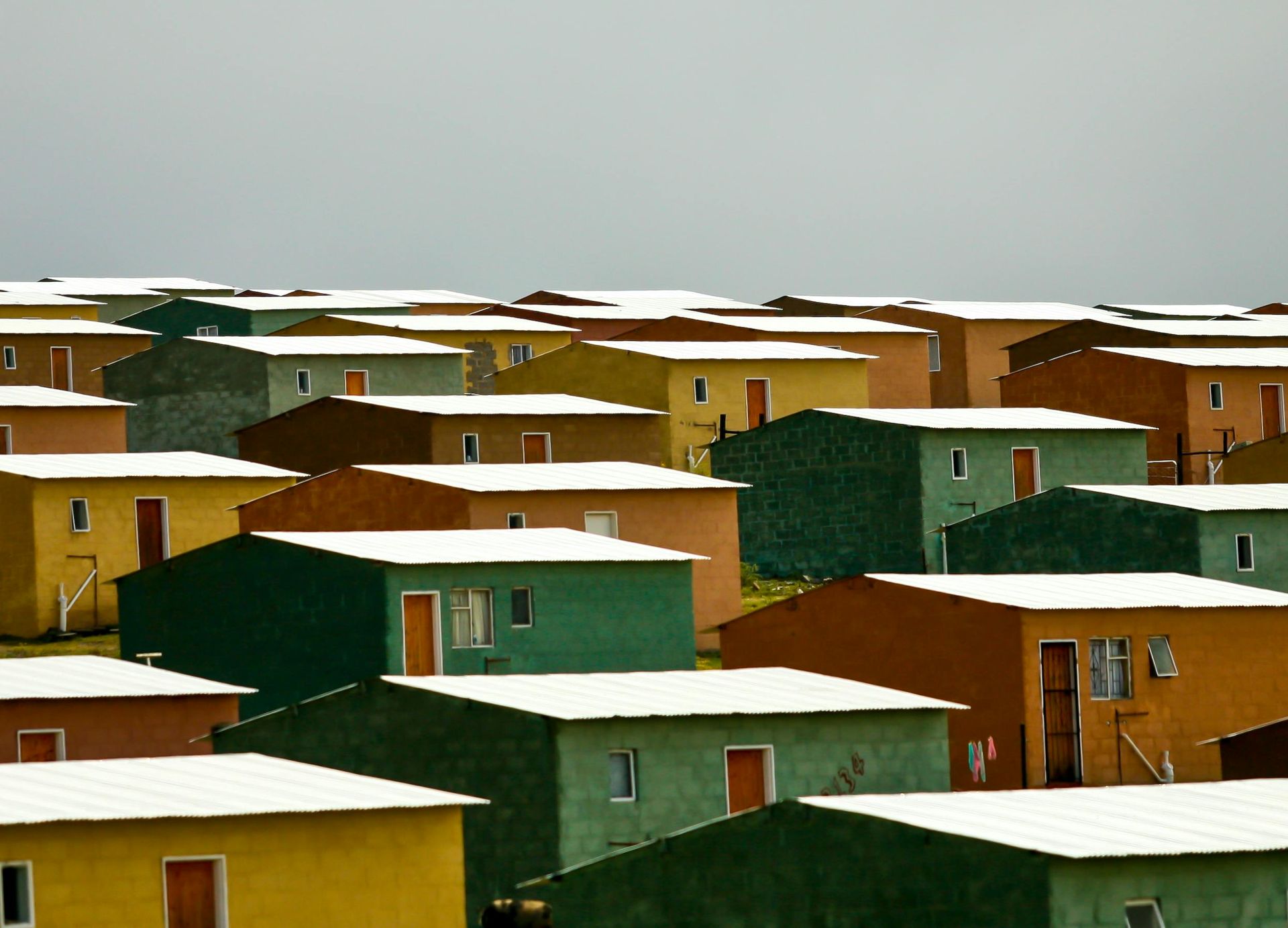 Rows of colorful, identical houses with white roofs under a gray sky.