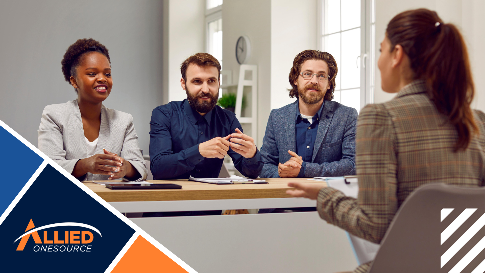 A temp job candidate sits across from three interviewers at a table in a brightly lit office.