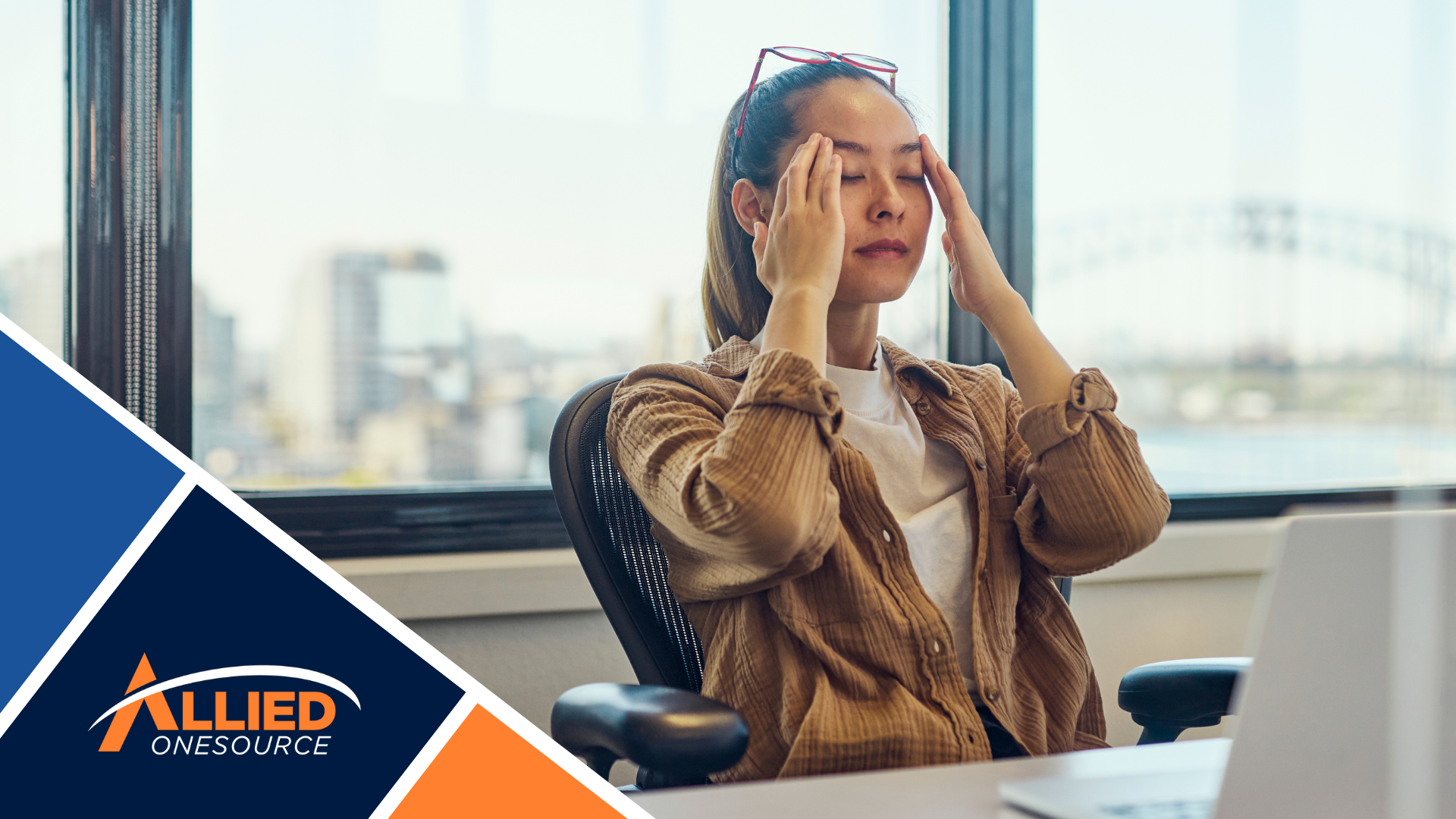 A woman sitting at a desk with her hands on her head.