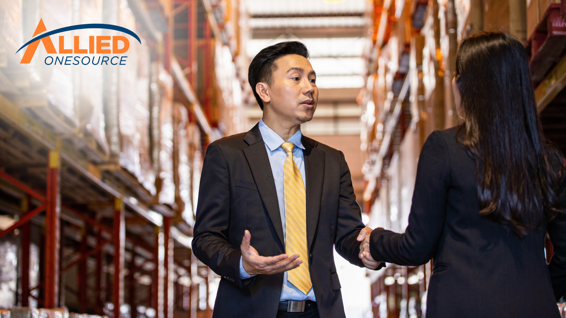  Two professionals are discussing hiring compliance and workforce decisions in a warehouse.