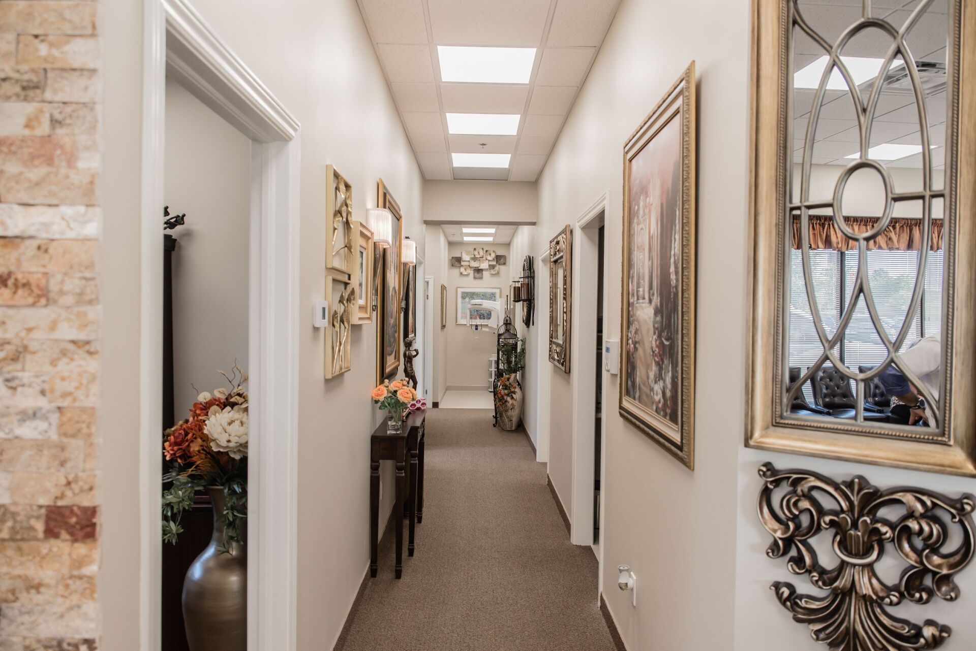 A long hallway with a mirror on the wall and paintings on the wall.