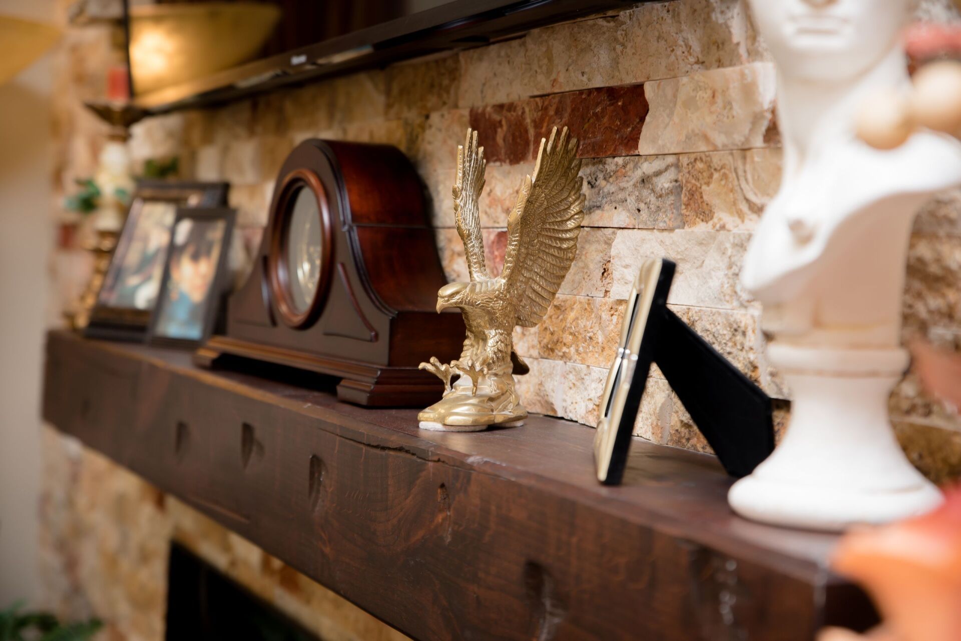A mantle with a clock , eagle statue , picture frames and a bust.
