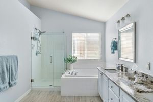Bright modern bathroom with glass shower, soaking tub, double vanity, and window blinds