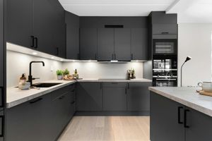Modern dark-gray kitchen with built-in cabinets, under-cabinet lighting, and a light wood floor