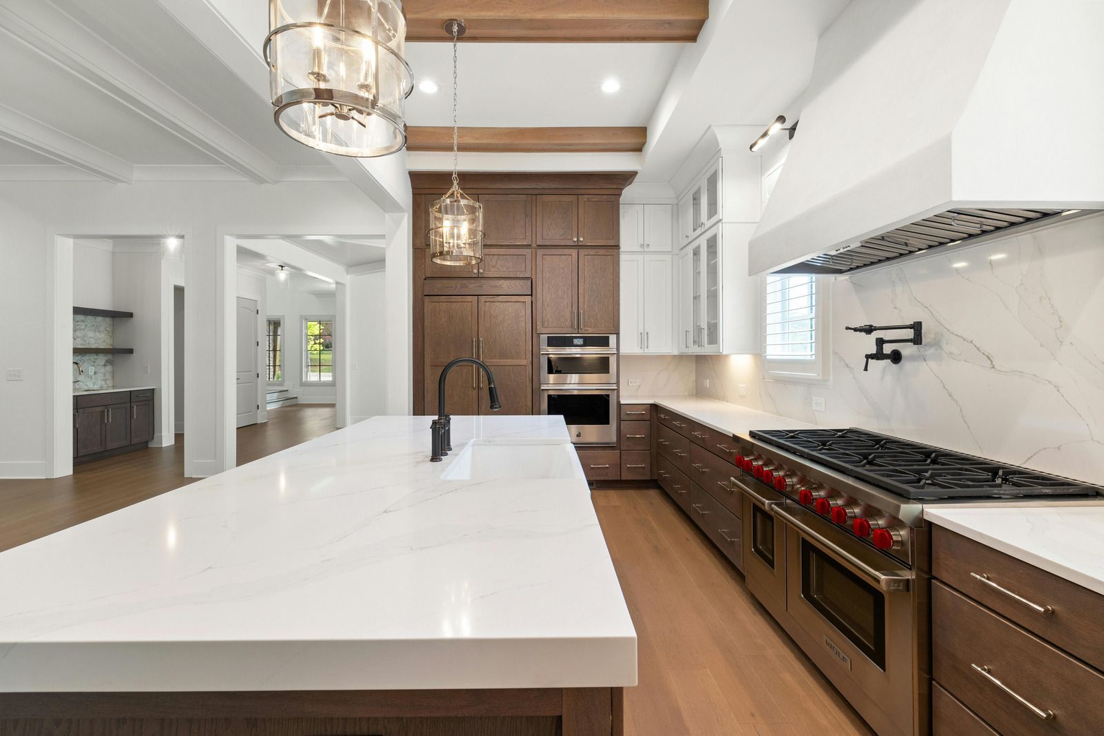 Modern white kitchen with large island, wood cabinetry, pendant lights, and stainless steel appliances.
