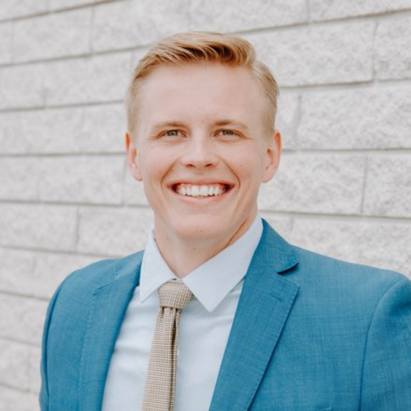 A man in a suit and tie is smiling in front of a brick wall