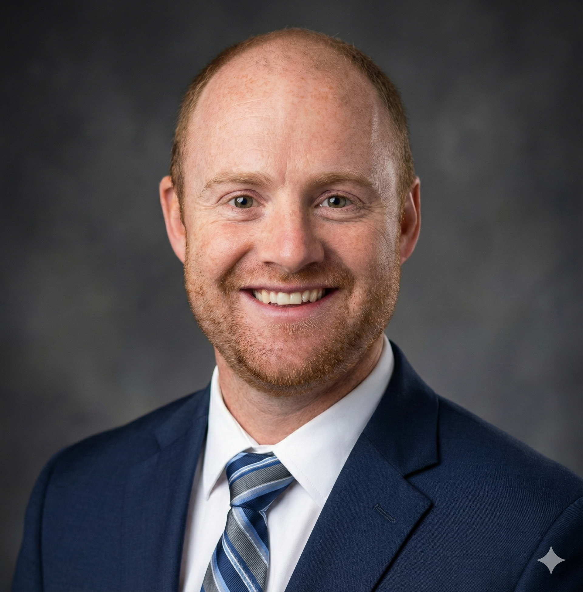 A man in a suit and tie is smiling in front of a brick wall
