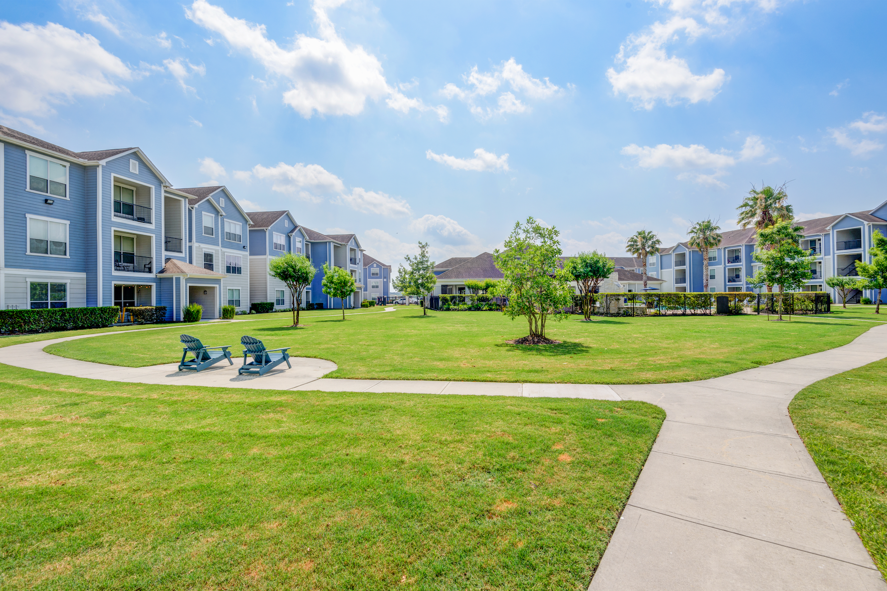 Apartment complex with brick and tan siding, chimneys, balconies, green lawn, and blue sky.