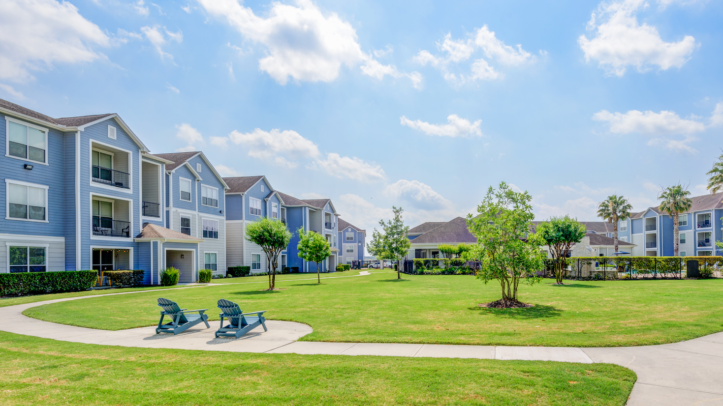 A row of apartment buildings with a large lawn in front of them.