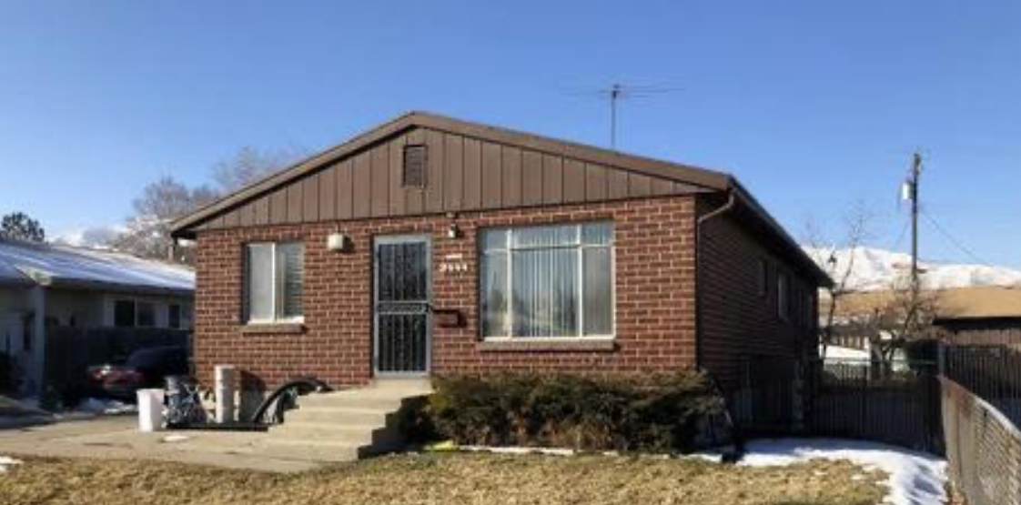 A small brick house with a brown roof and a car parked in front of it.