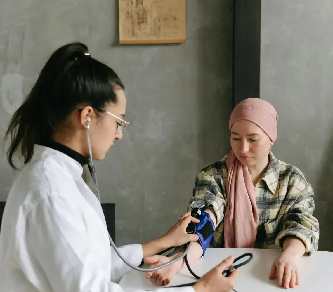 Clinician taking blood pressure of a patient seated at a white table in a gray room