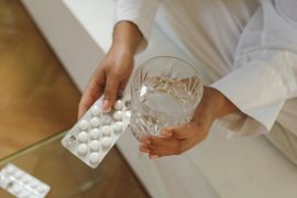 Hands holding a pill blister pack and a glass of water on a white couch