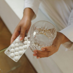 Hands holding a blister pack of tablets and a clear glass of water