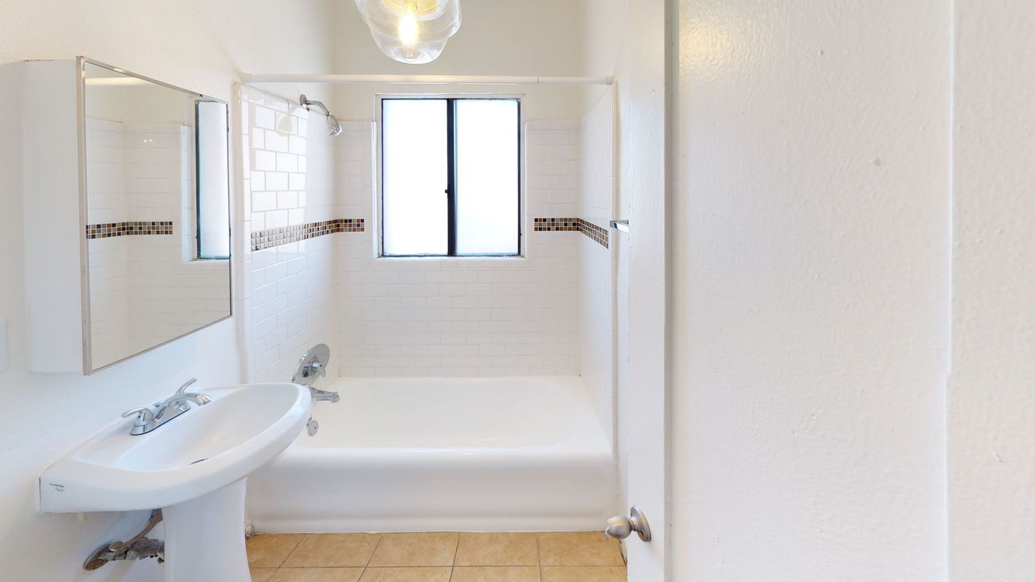Bathroom with a white tub and sink, a window, and a light fixture.