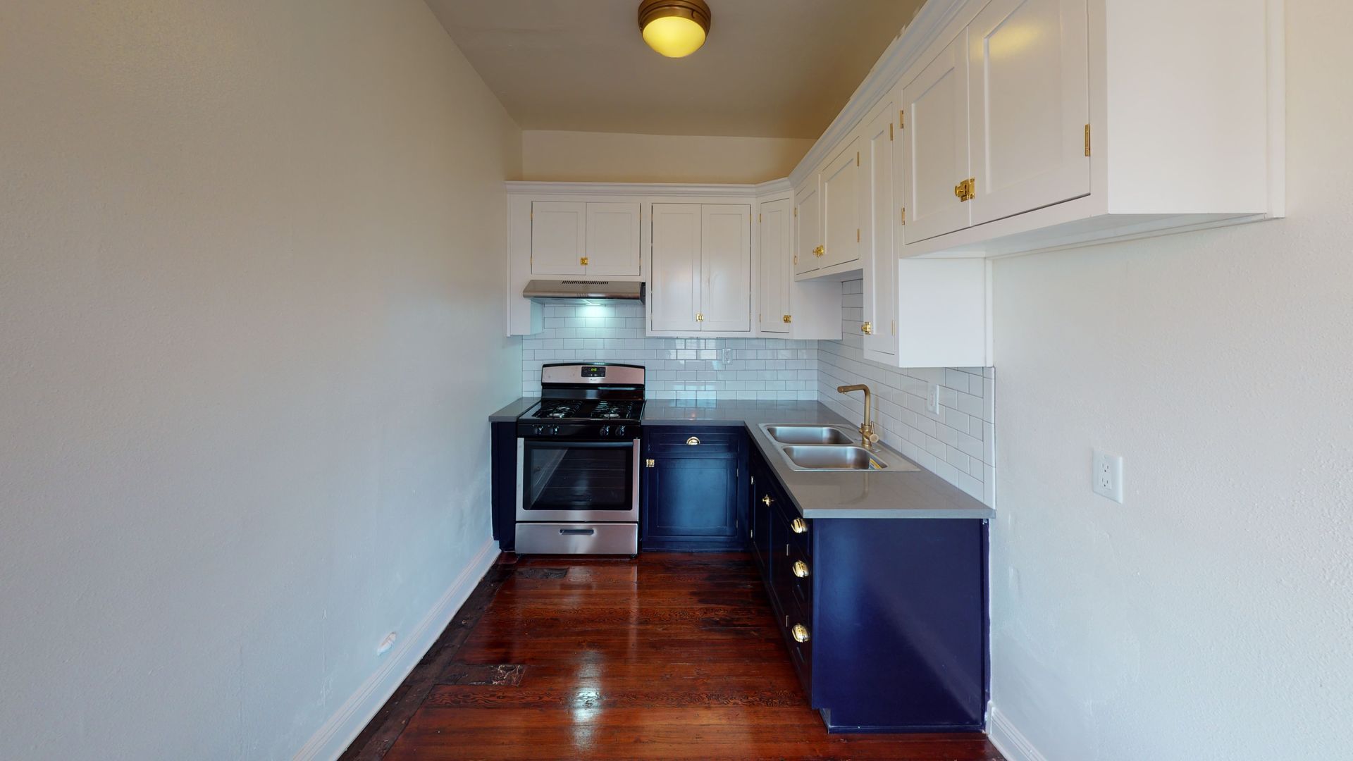 Small kitchen with white and blue cabinets, stainless steel appliances, and wooden floor.