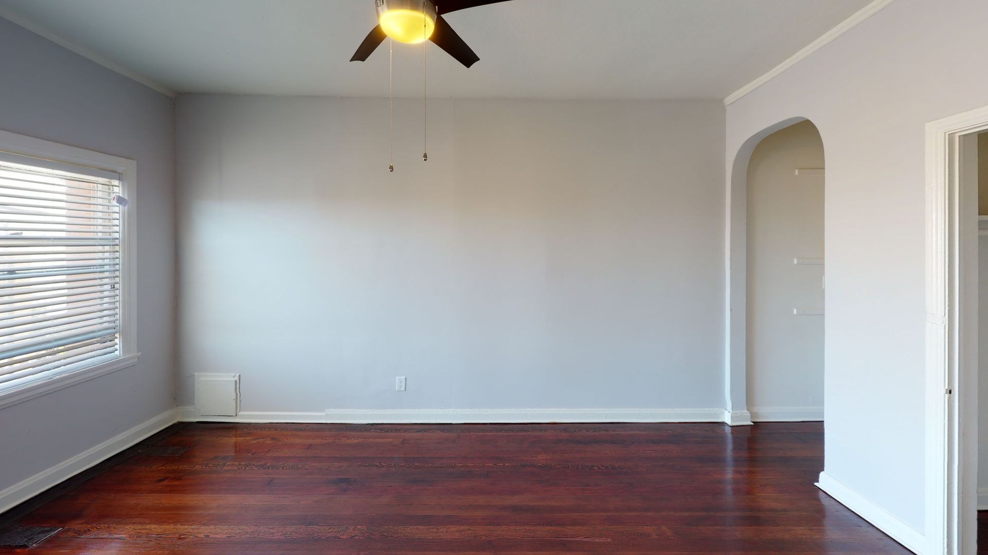 Empty room with hardwood floors, light gray walls, window, and arched doorway.