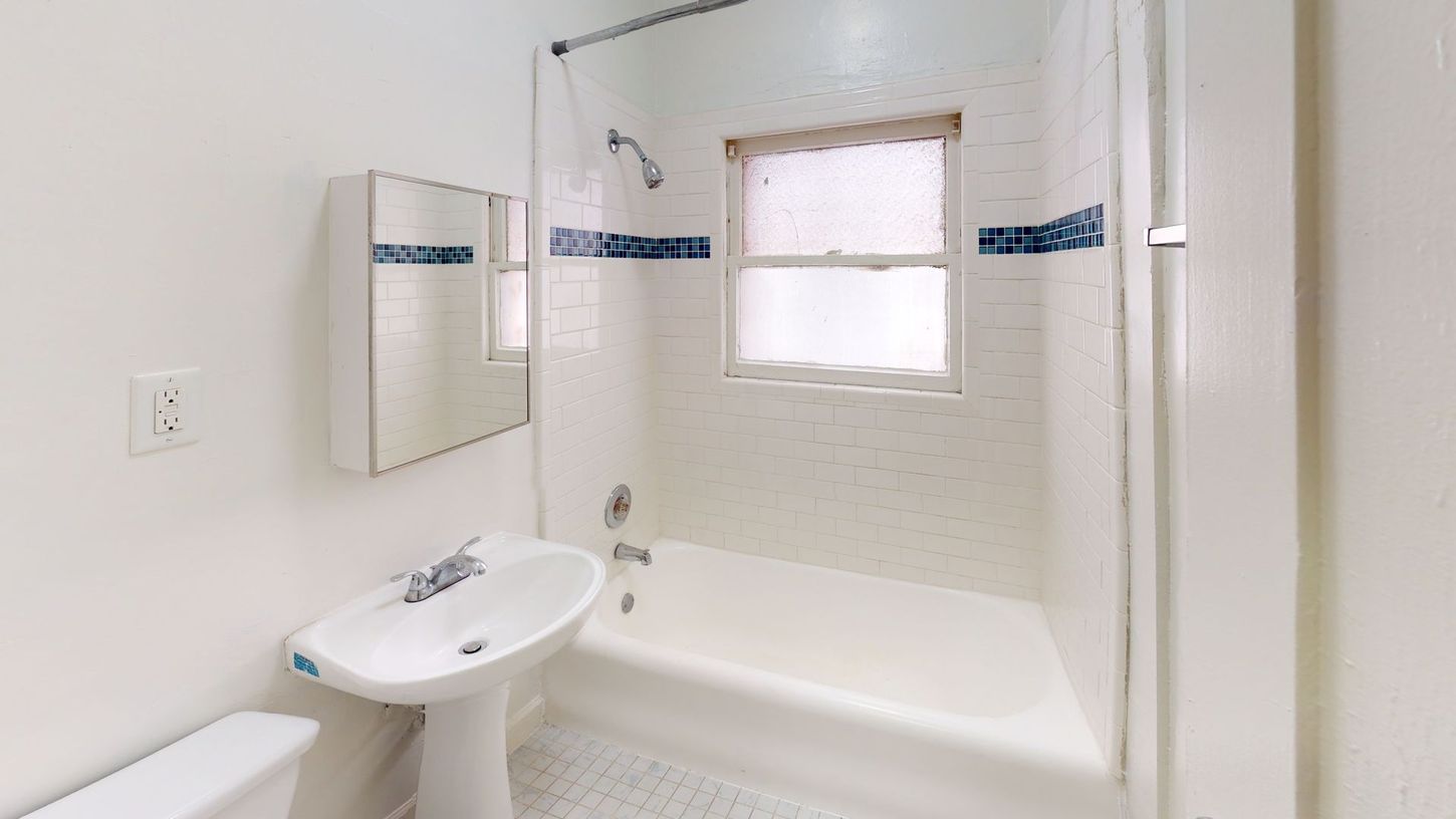 White bathroom with tub, sink, mirror, and window with blue tile accents.