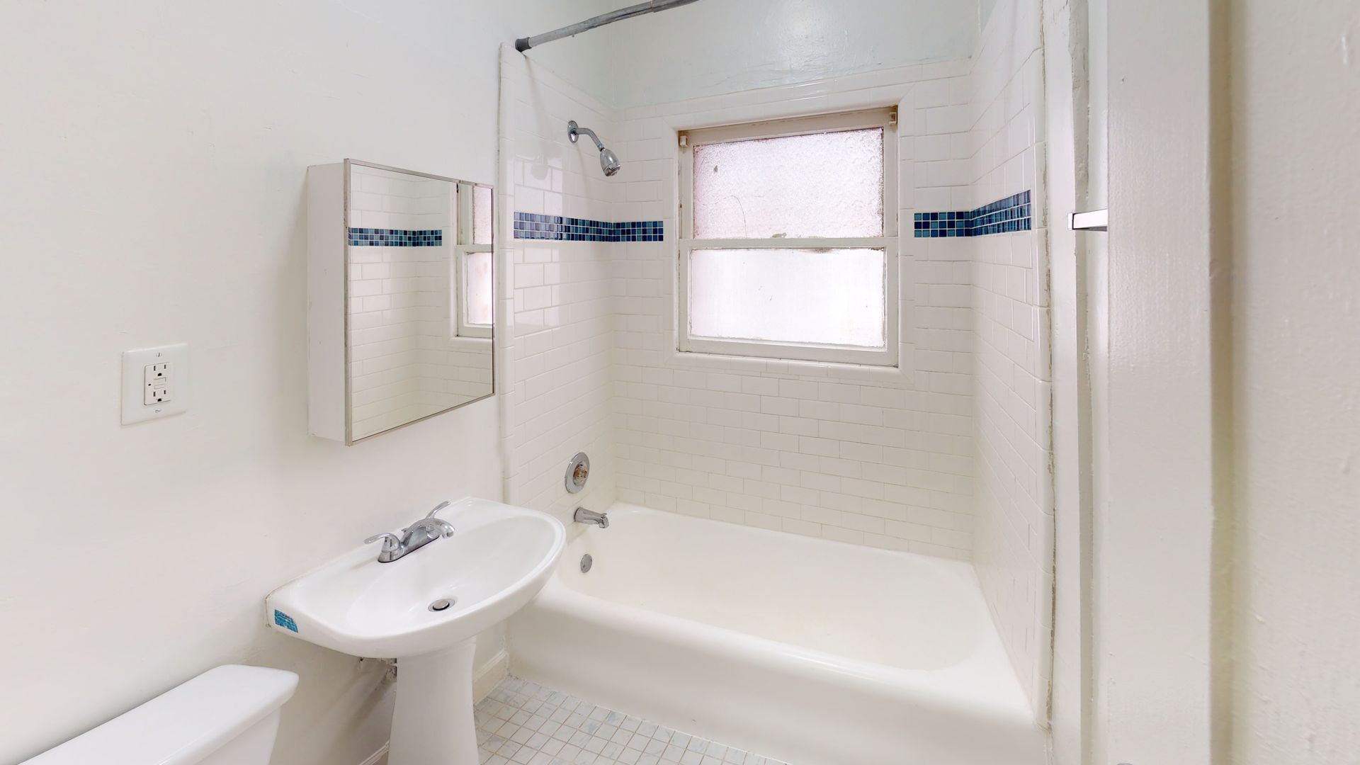 White bathroom with tub, sink, mirror, and window with blue tile accents.