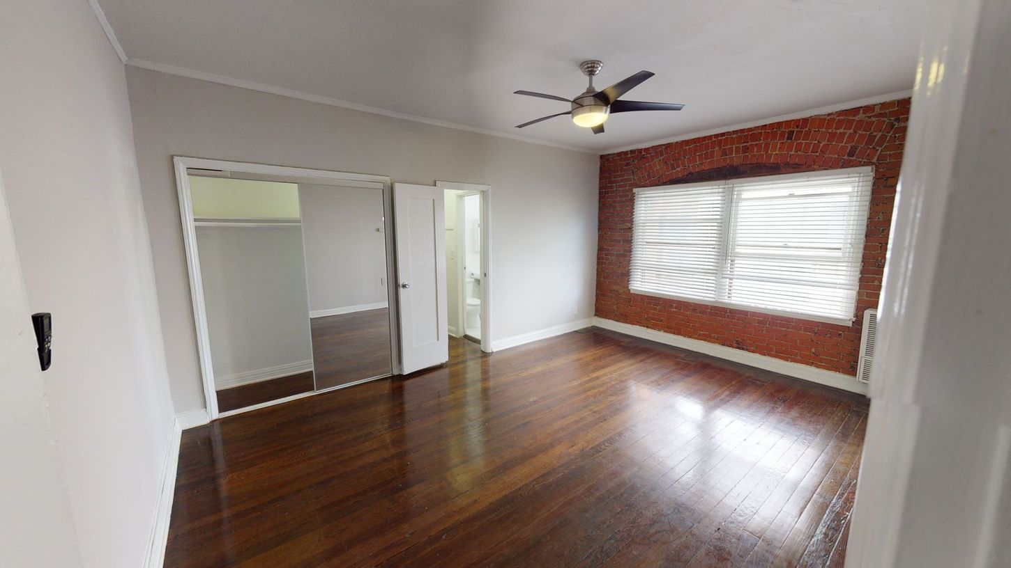 Empty room with hardwood floors, exposed brick wall, and sliding closet doors.