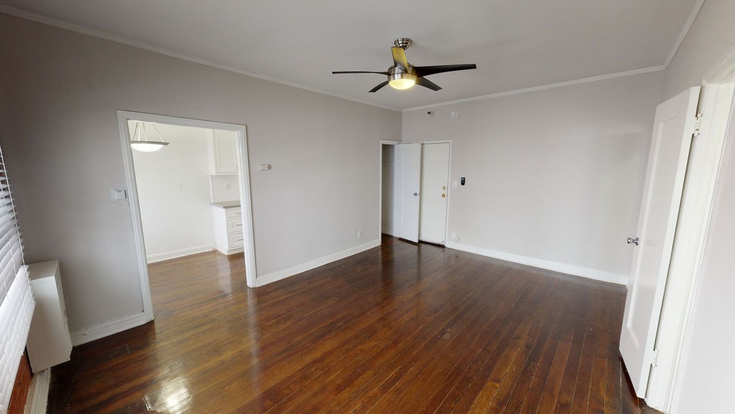 Empty room with hardwood floors, light gray walls, white doors, and a ceiling fan.