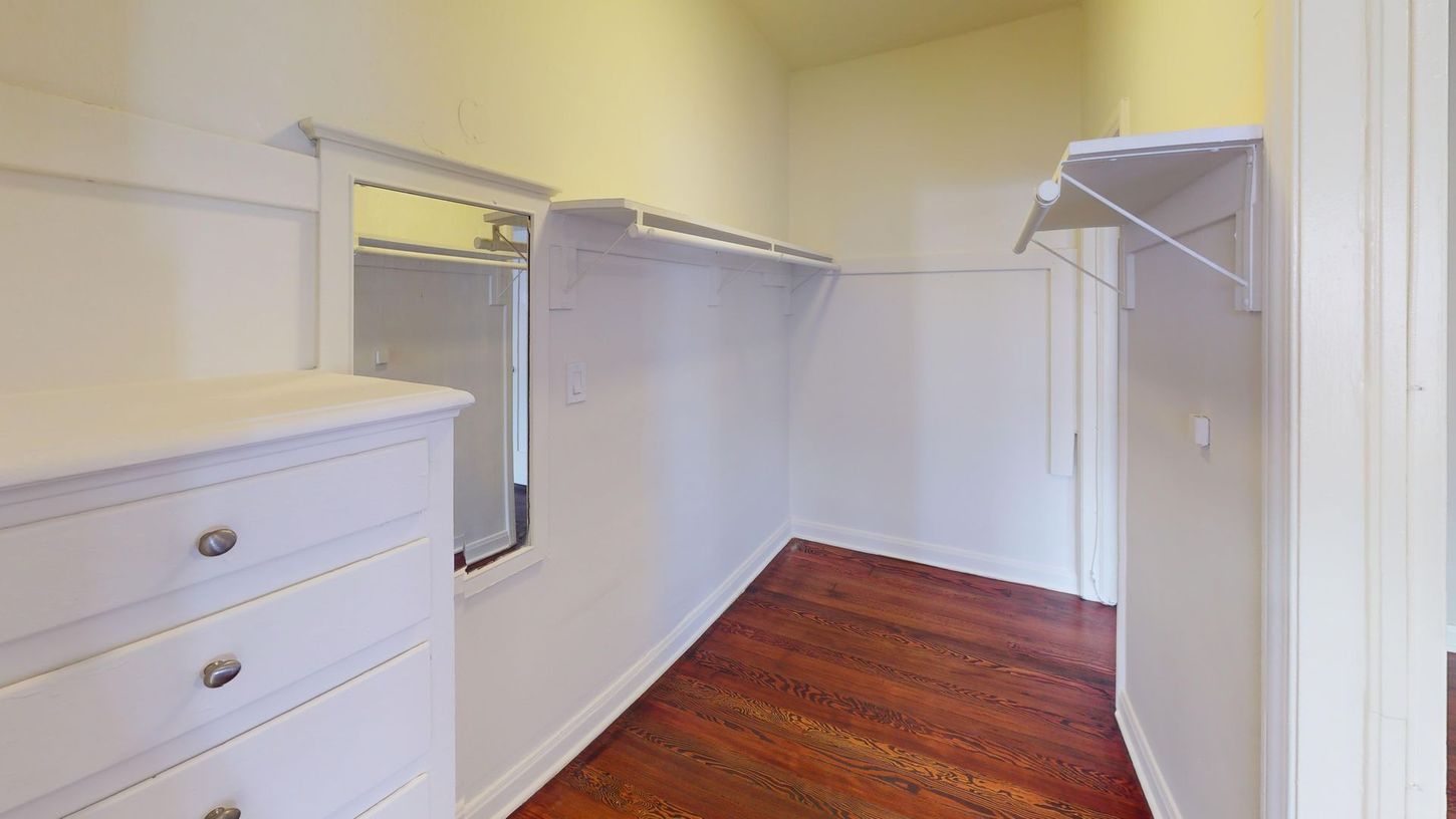 Walk-in closet with white shelves and dresser, dark wood floor, and a window with a mirror.