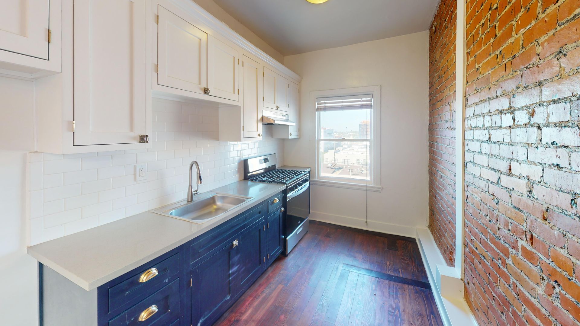 Kitchen with white cabinets, blue cabinets, brick wall, and a window.