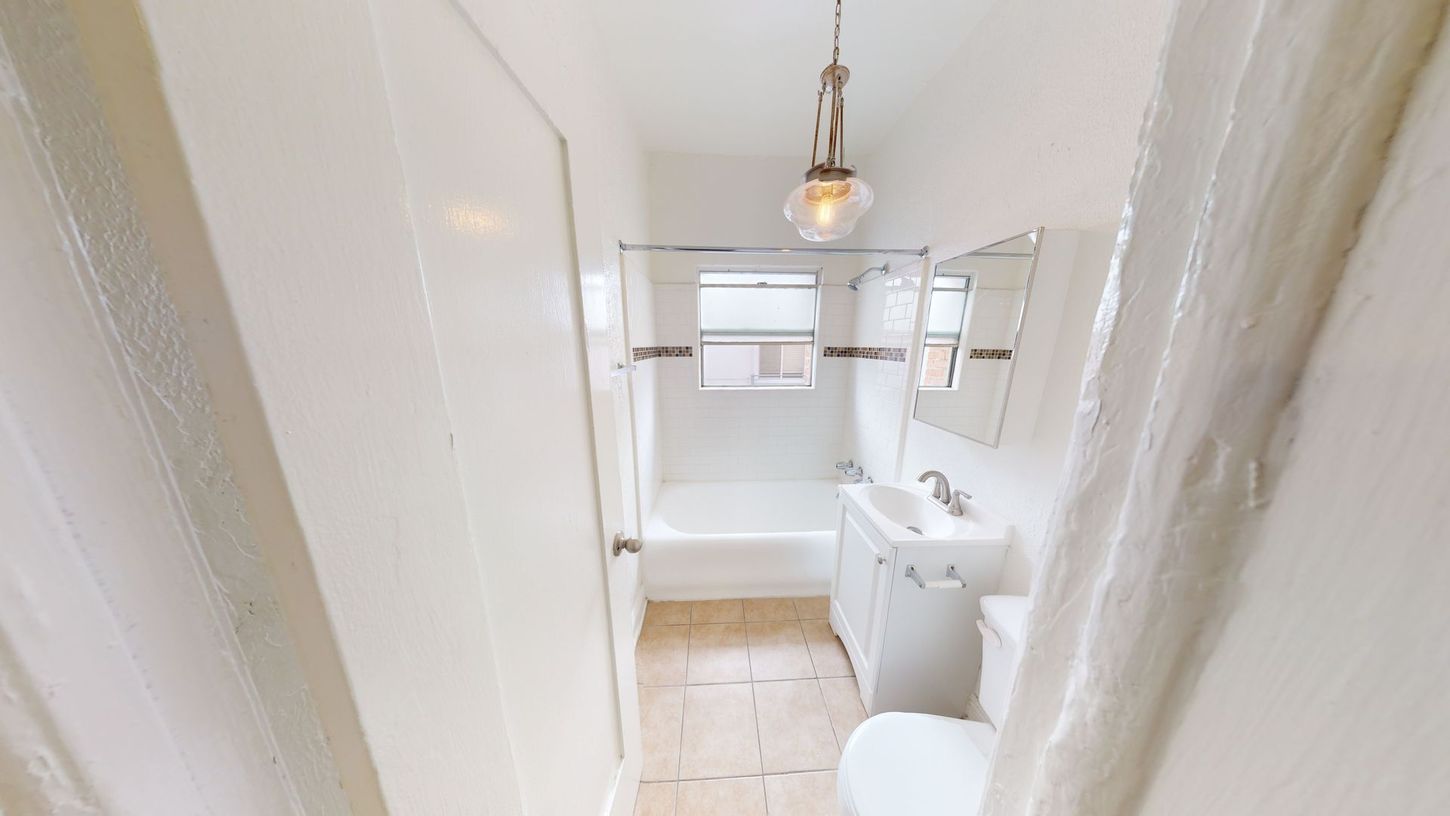 Small, white bathroom with tub, toilet, and sink; a light fixture hangs from the ceiling.