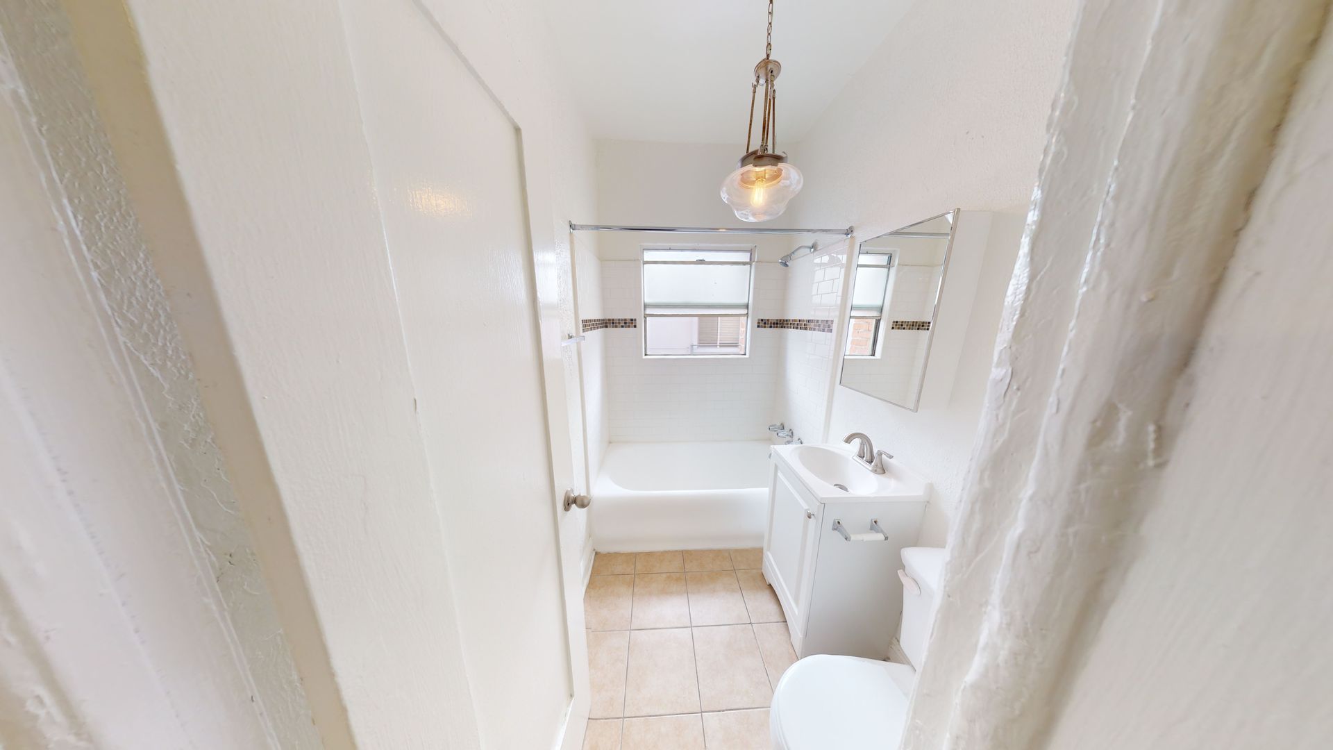 Small, white bathroom with tub, toilet, and sink; a light fixture hangs from the ceiling.