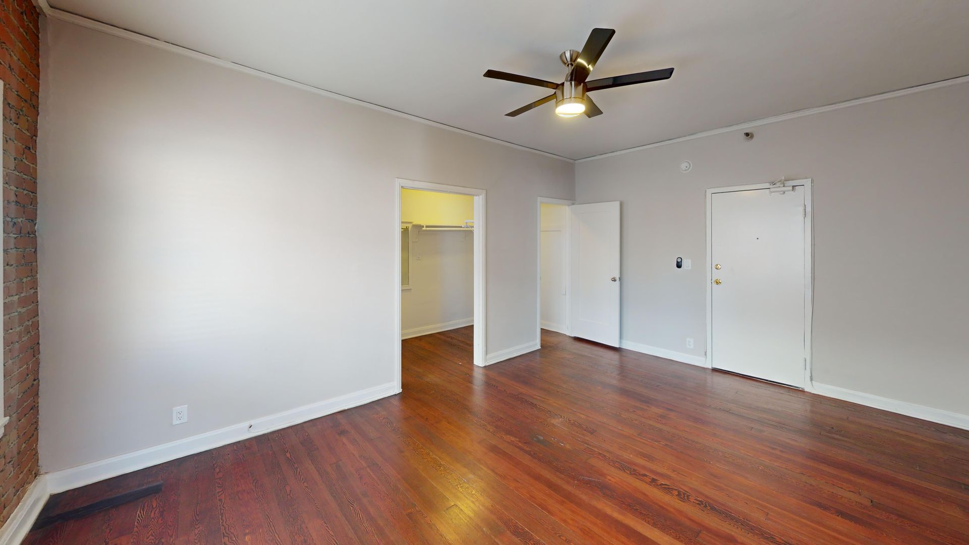 Empty room with hardwood floors, white doors, and a ceiling fan.
