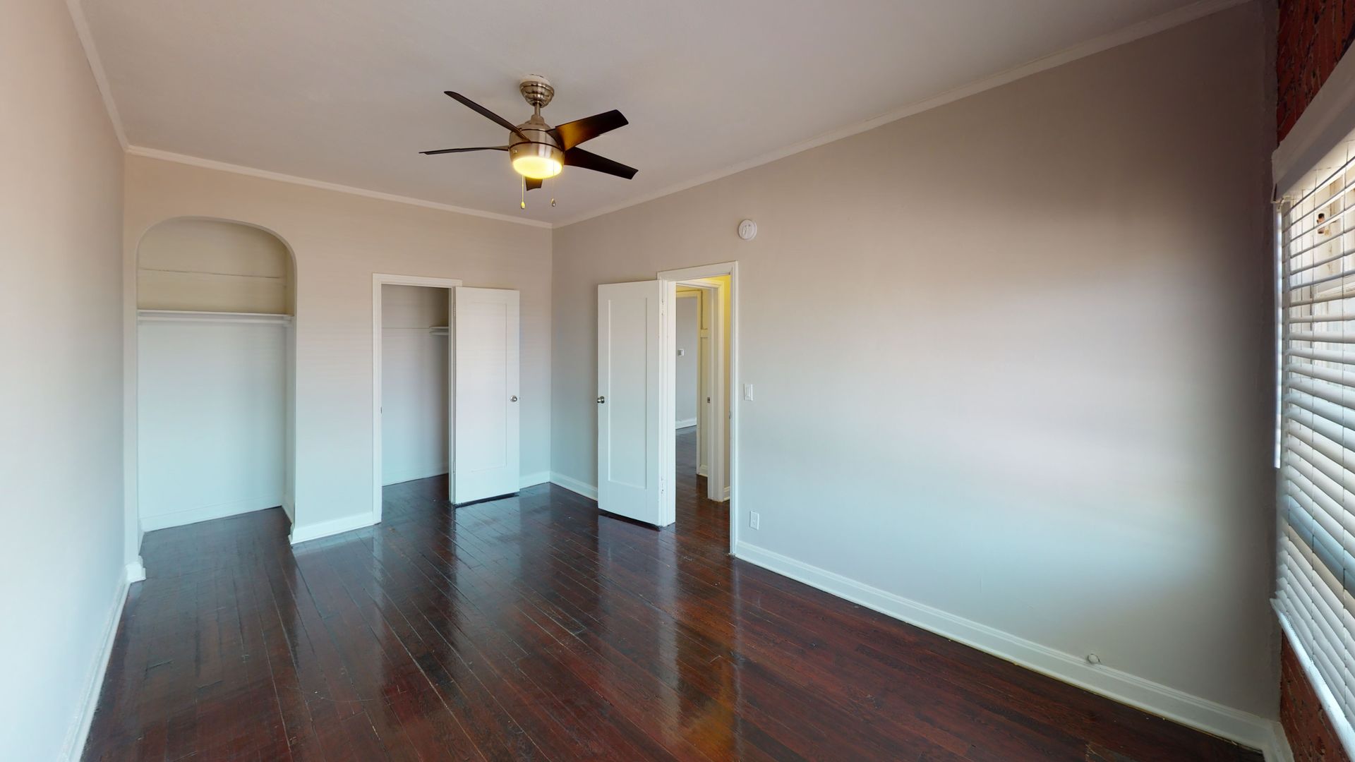 Empty bedroom with dark wood floors, light walls, ceiling fan, and open closet doors.
