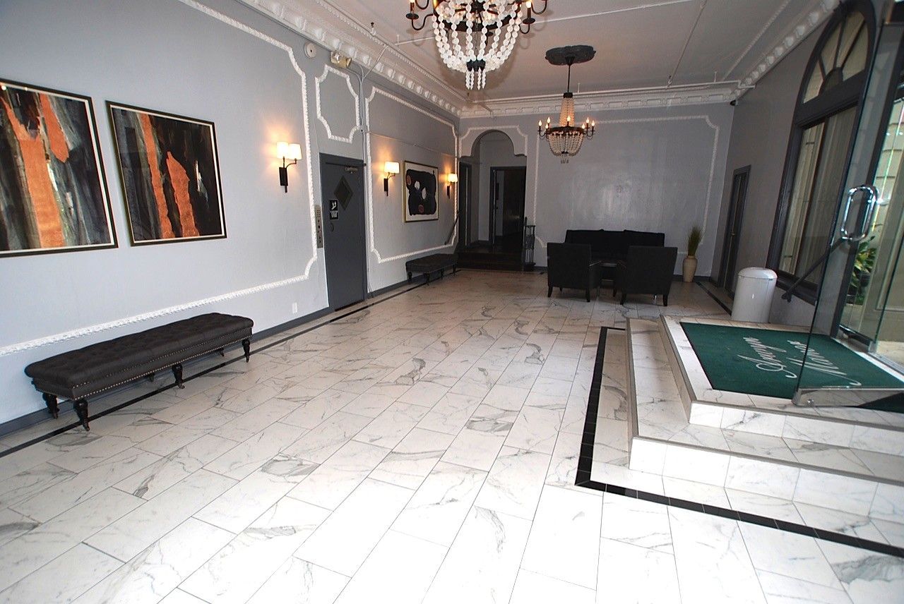 Elegant lobby with marble floor, gray walls, artwork, chandeliers, and seating.