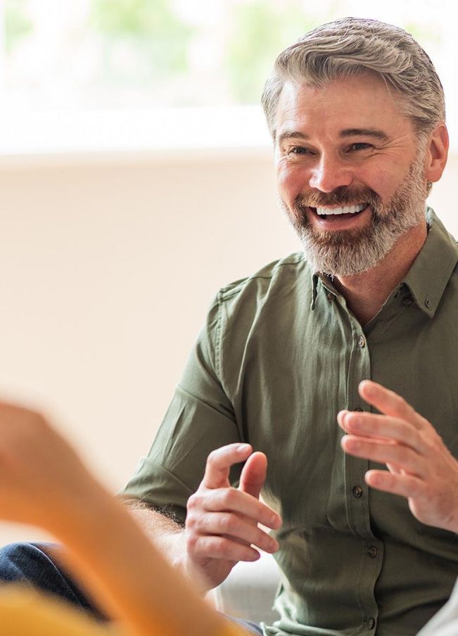a man with a beard is smiling while talking to another man .