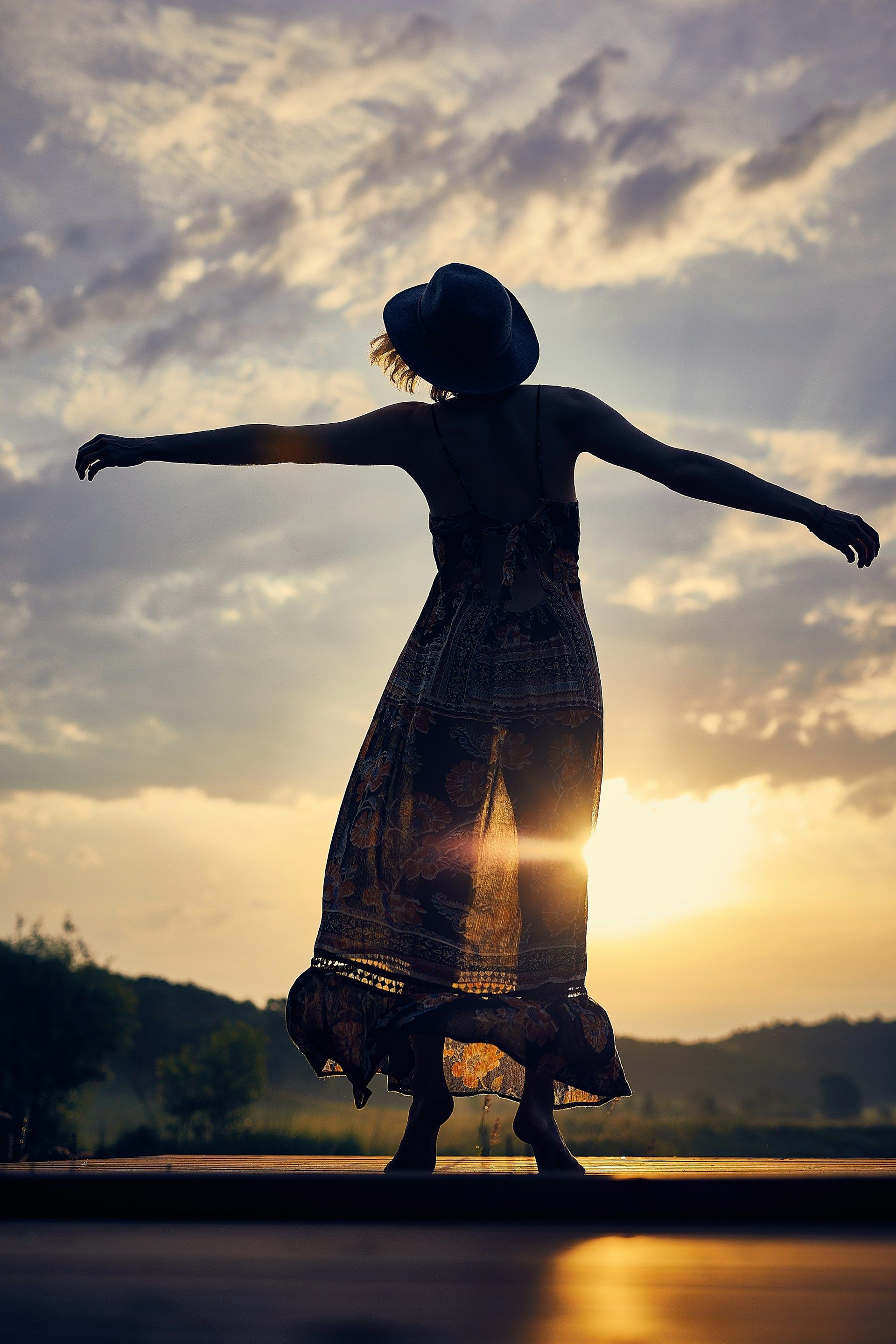 a woman in a dress and hat is dancing at sunset