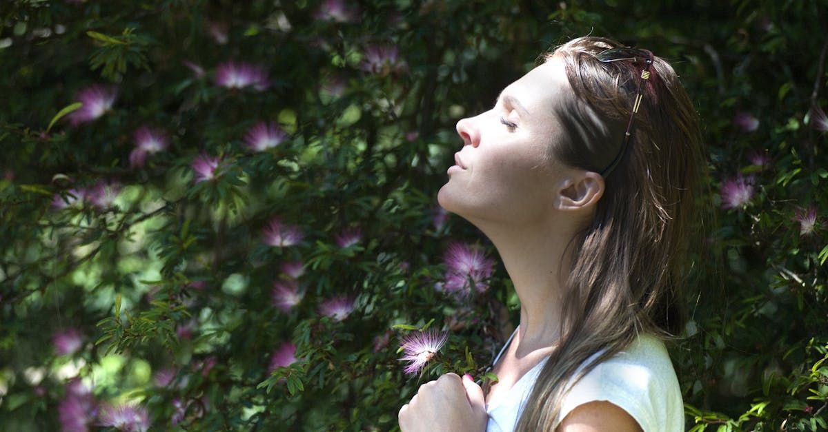 A woman is standing in front of a bush with her eyes closed.