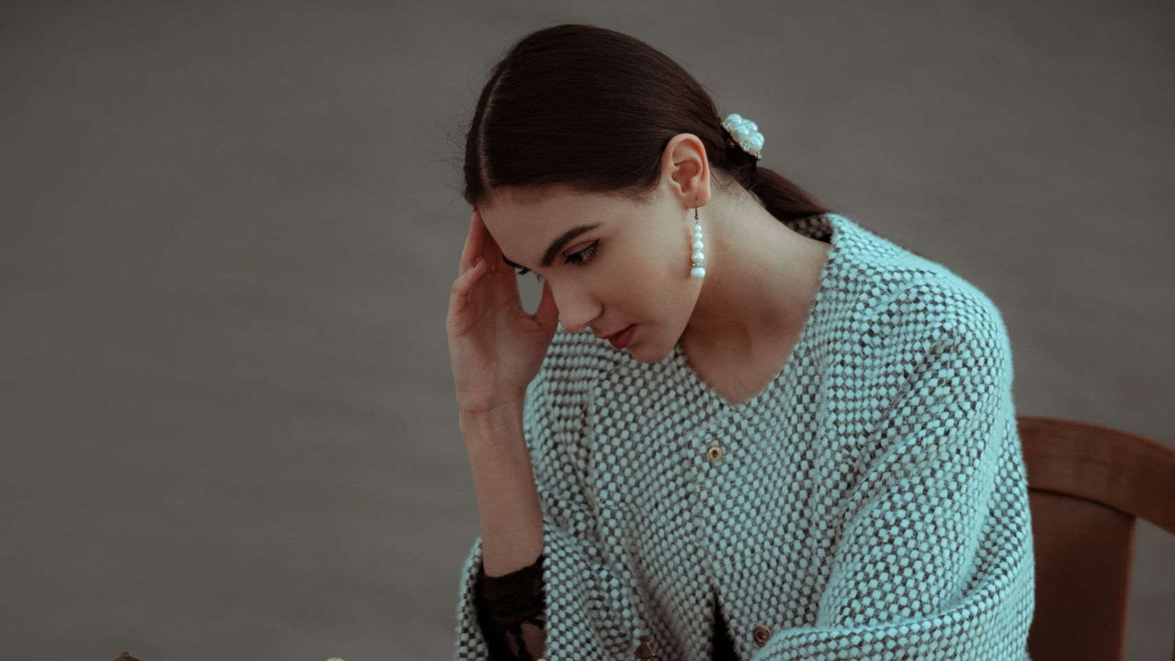 a woman wearing pearl earrings holds her head