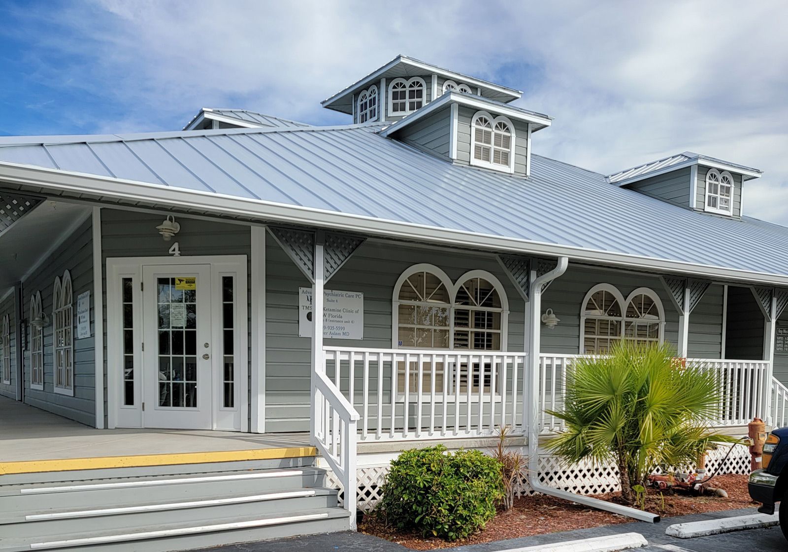 A gray building with a silver roof and a white porch