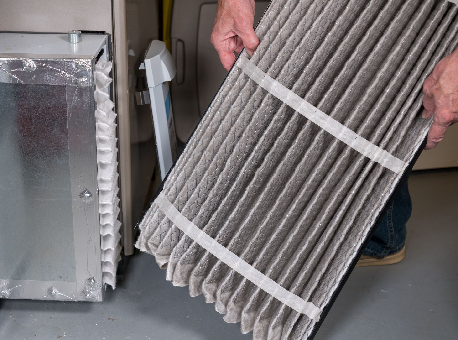 A person is holding a dirty air filter in front of an air conditioner.