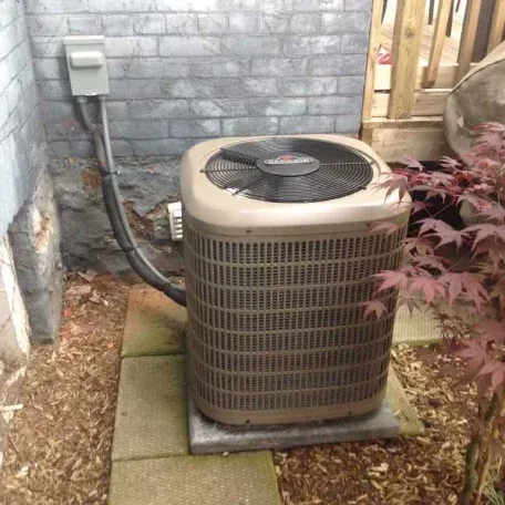 An air conditioner is sitting on a sidewalk next to a brick wall.