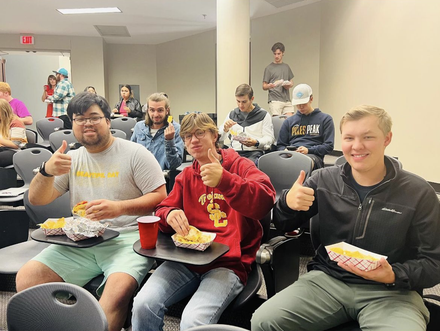 Three AMA students give the camera thumbs ups while eating free tacos.