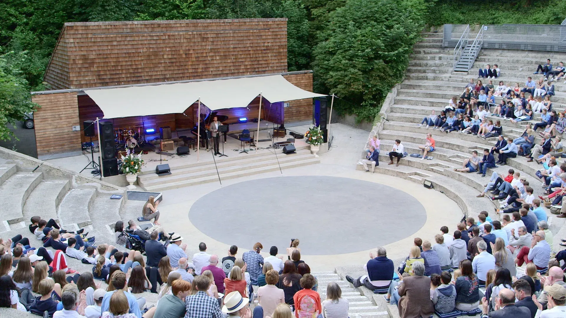 A large group of people are sitting in an amphitheater watching a concert.