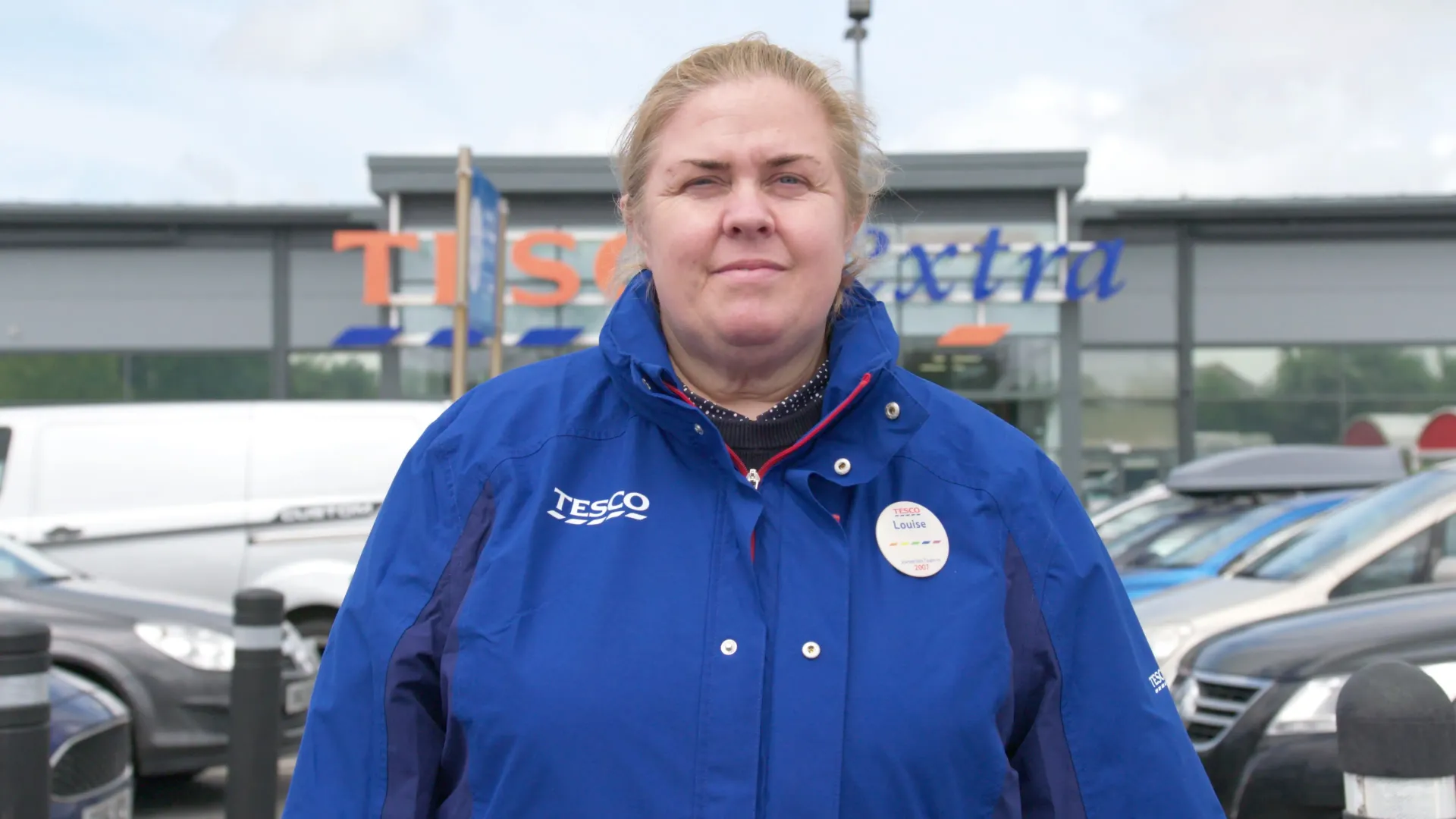A woman in a blue jacket is standing in front of a tesco store.