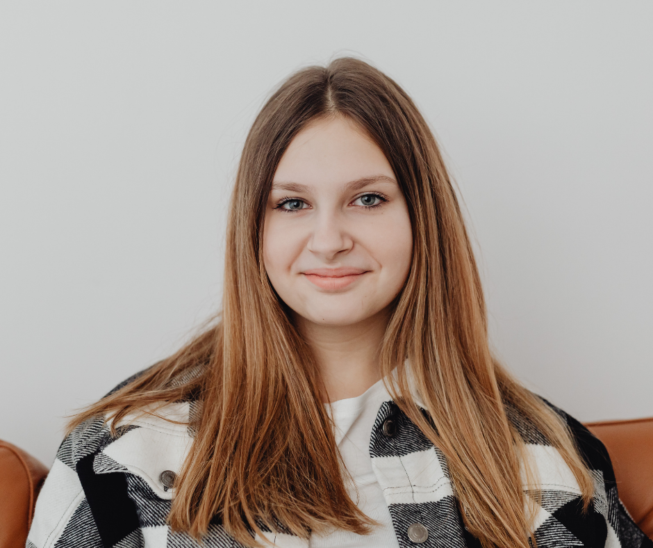 Woman with long, ombre hair smiles, wearing a white shirt and black and white plaid jacket.