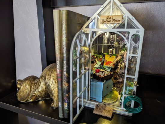 A greenhouse is sitting on top of a shelf next to a book.